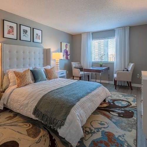 Downtown Nashville, TN, Apartments - Cumberland on Church - Bedroom with Plank Flooring, Decorative Area Rug, Large Bed with Nightstands, and a Table and Chair by A Window